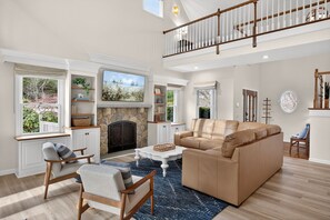 Un salon spacieux avec un haut plafond, une cheminée, une grande fenêtre et un balcon.