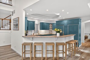 A modern kitchen with teal cabinets, a granite countertop, and wooden stools.
