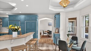 Una cocina moderna con armarios azules, encimera de granito y comedor con mesa y sillas de vidrio.