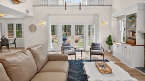 Amplia sala de estar con techo alto, sofá de cuero, una mesa de centro y vistas al exterior a través de grandes puertas correderas.