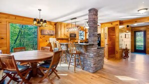 Interior de cabana de madeira com área de refeições, cozinha e lareira de pedra.