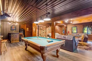 A pool table in a room with wooden walls and ceiling, a bar area, and a seating area with a view of the outdoors. - Riverfront Escape - Hot Tub • Game Room • Fire Pit (Ellijay)