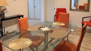 Un comedor con una mesa de vidrio, sillas naranjas, un reloj en la pared y un espejo que refleja la habitación.