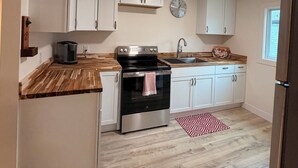 Una cocina moderna con armarios blancos, horno de acero inoxidable, cafetera y un reloj en la pared.