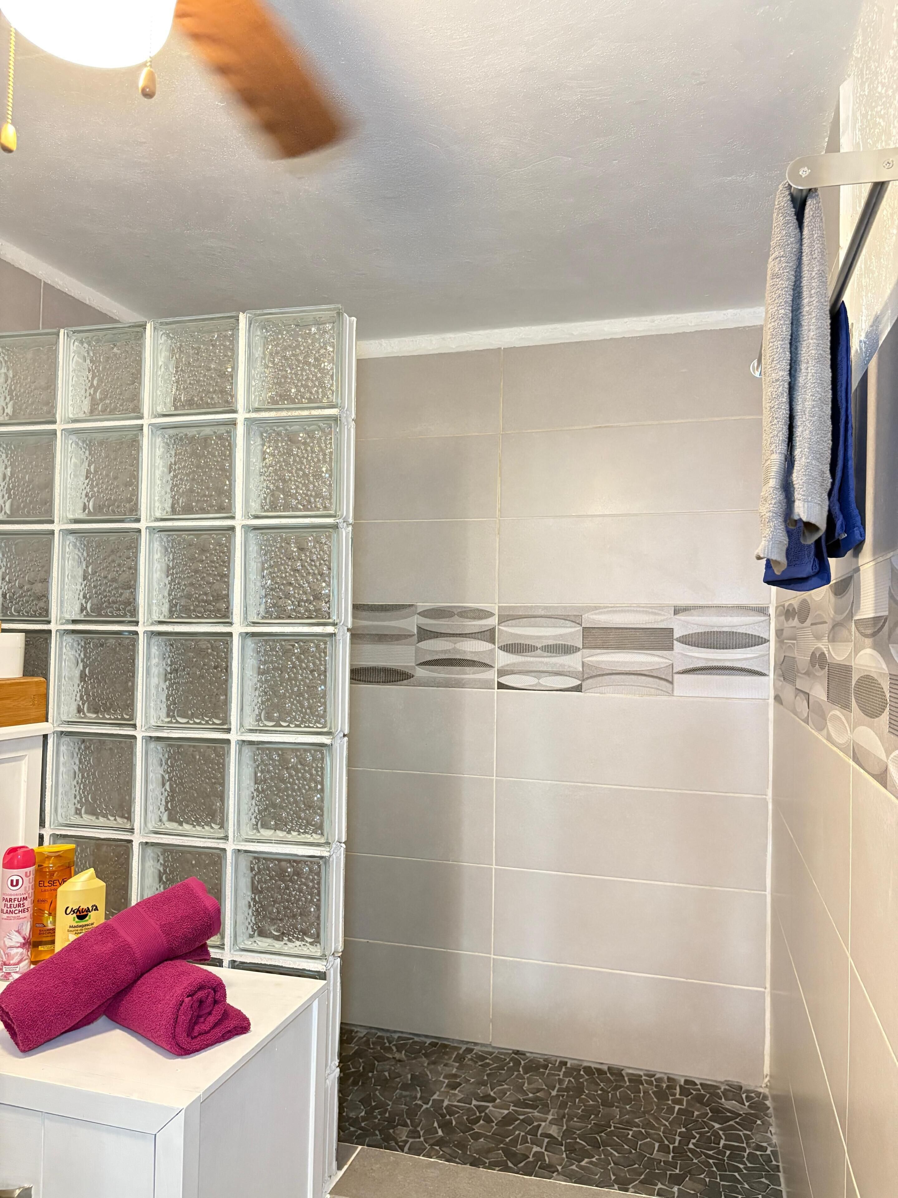 A bathroom with a glass block wall, tiled shower, and a white sink with a pink towel.