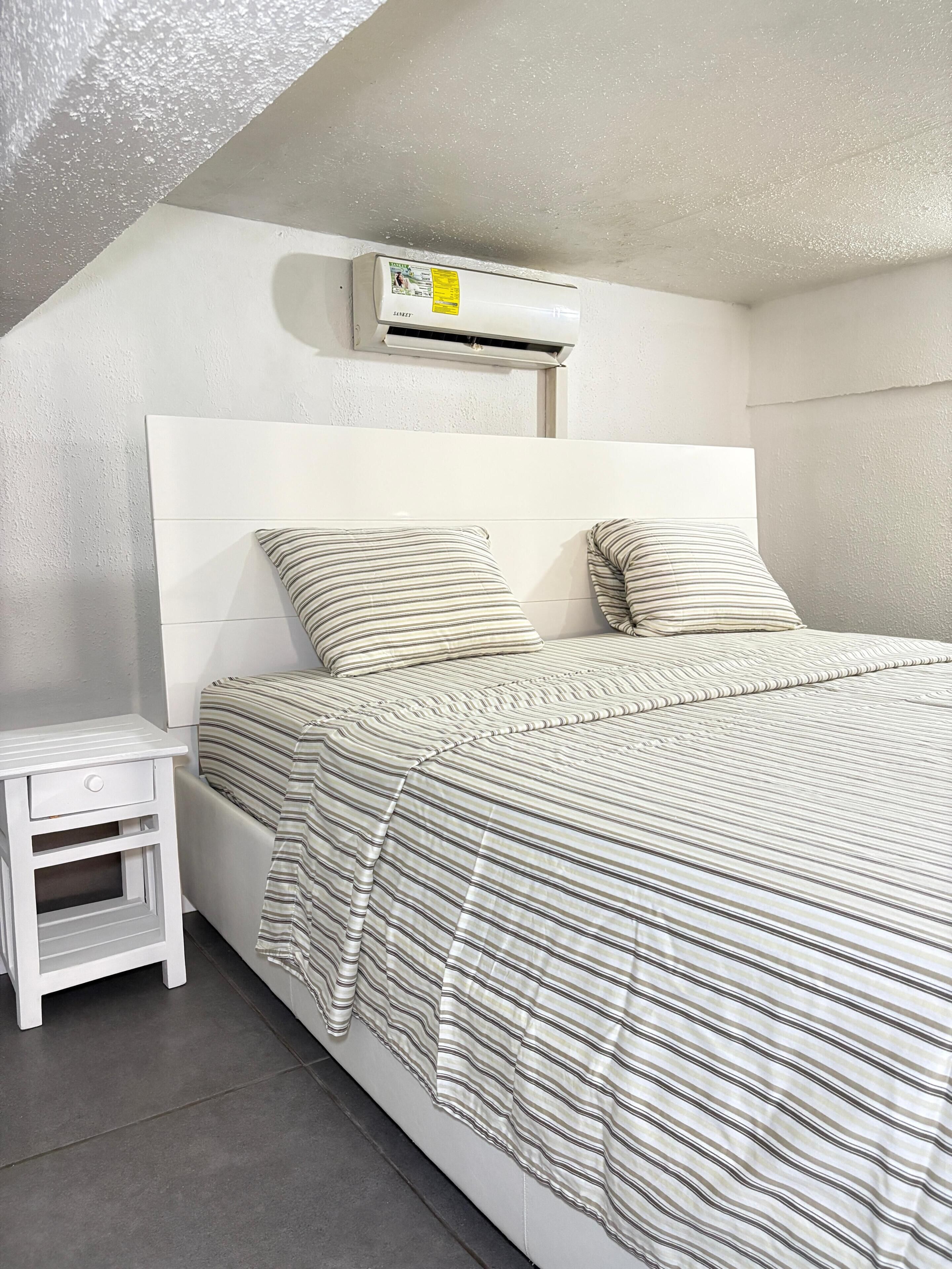 Une chambre à coucher comprenant un lit, une table de chevet et un appareil de climatisation.
