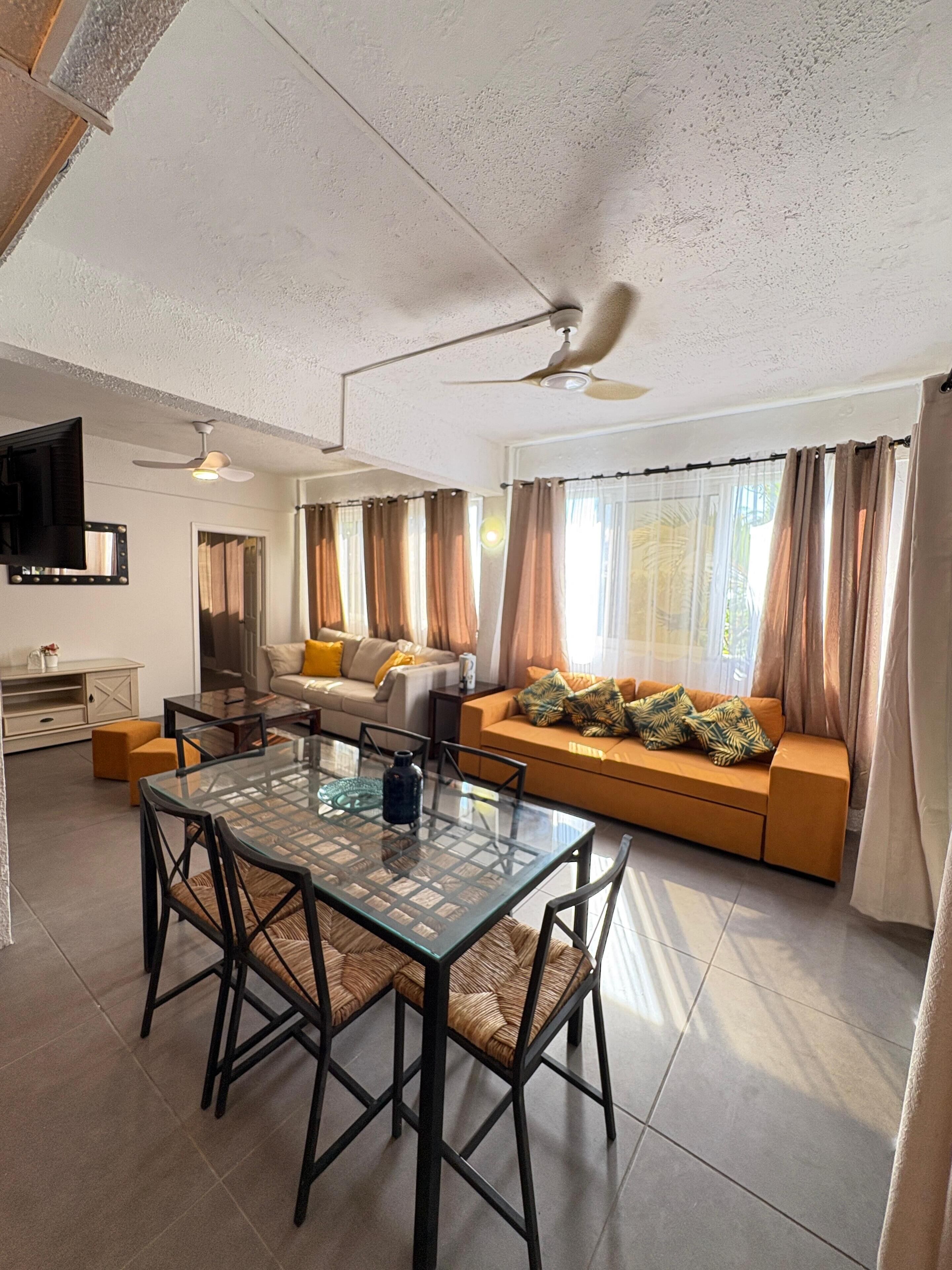 A modern living room with a glass dining table, sofa, and a ceiling fan.