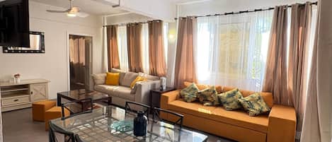A modern living room with a glass dining table, sofa, and a ceiling fan.