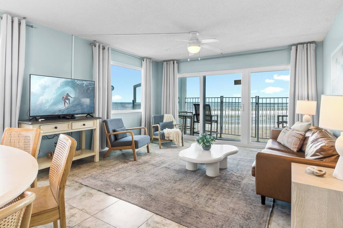 A living room with a TV, seating, a coffee table, and a balcony with a view.