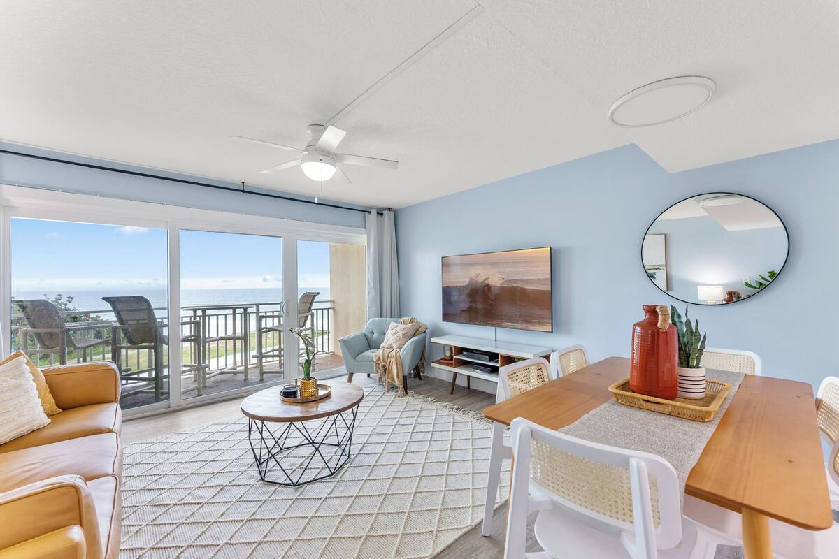 A spacious living area with a balcony, a television, and a dining table.