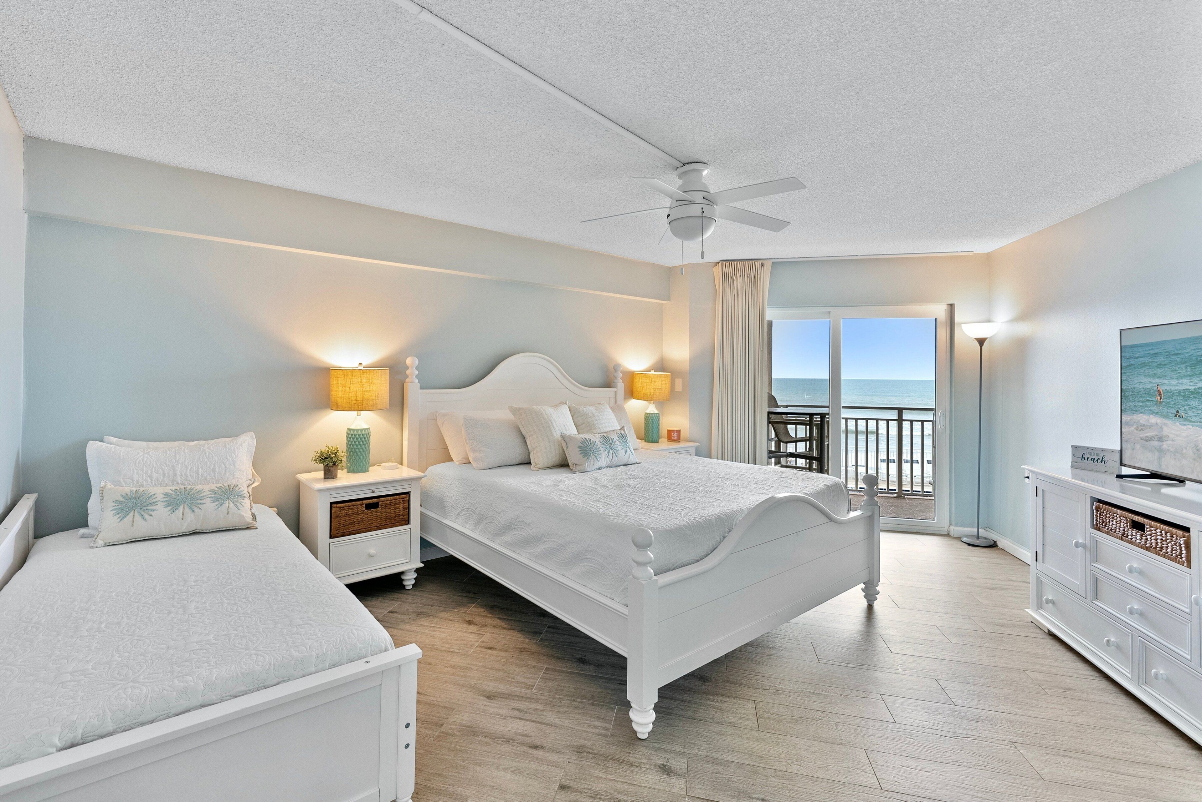 A hotel room with a bed, bedside tables, a TV, and a balcony with a view of the sea.
