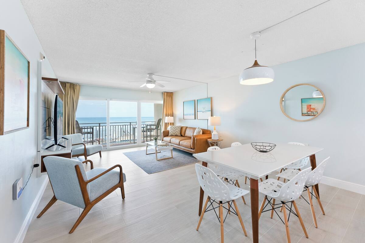 A modern living room with a dining area, a sofa, and a view of the ocean.