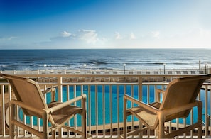 A poolside view with two wicker chairs, a clear blue pool, and a view of the ocean.