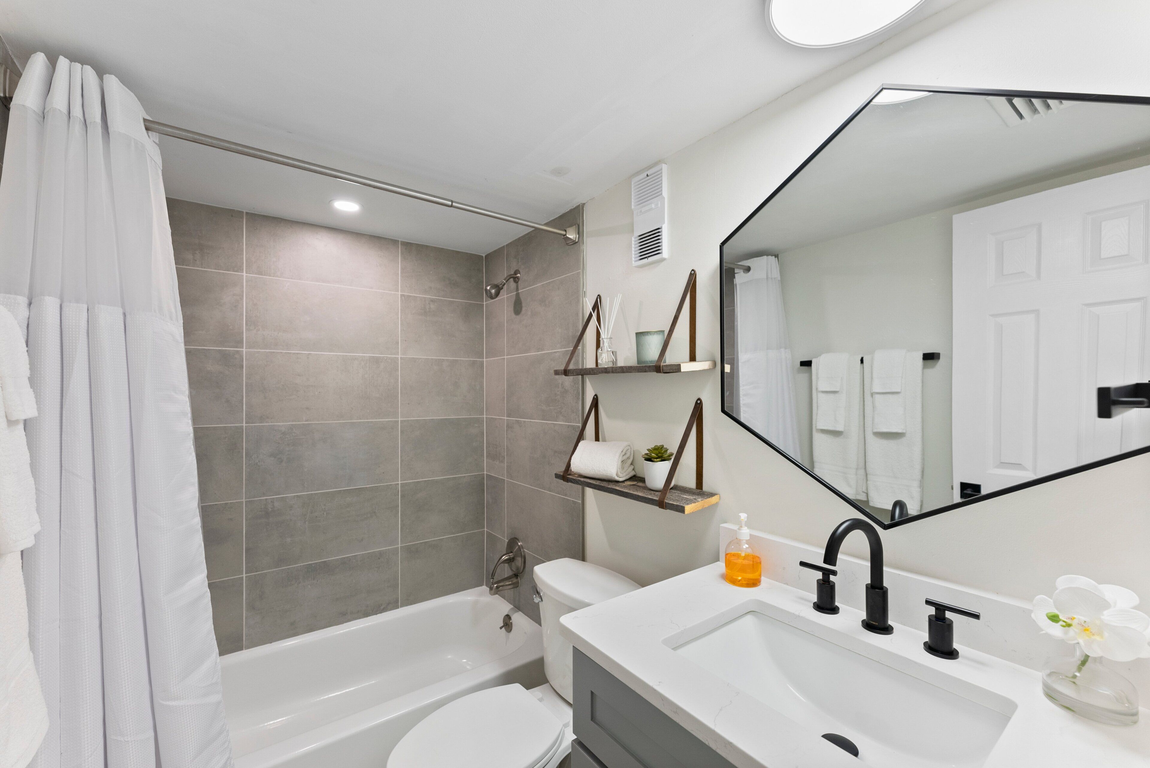 A modern bathroom with a bathtub, toilet, and sink, featuring a large mirror and a shower curtain.
