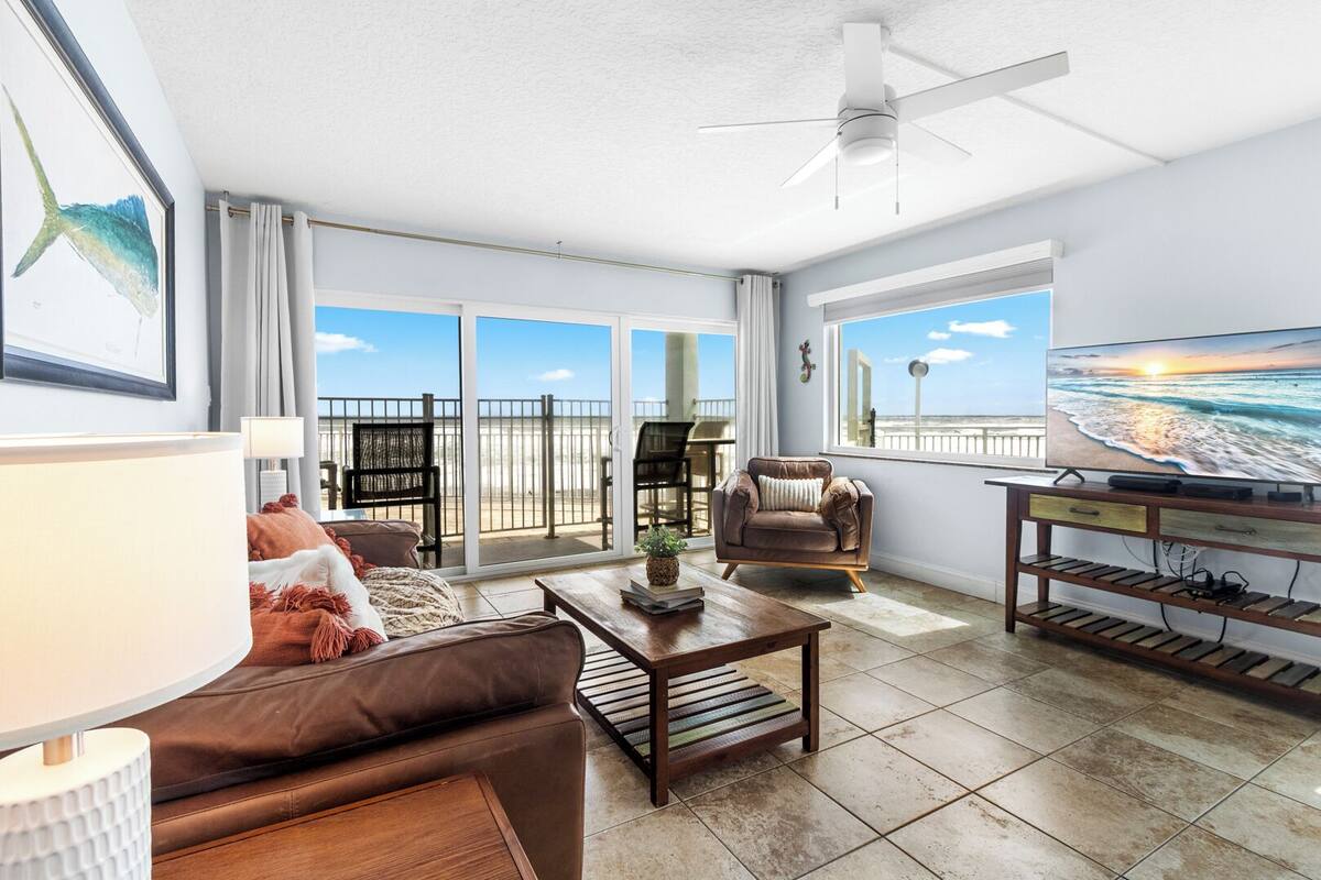 A spacious living area with a balcony, a ceiling fan, and a television.