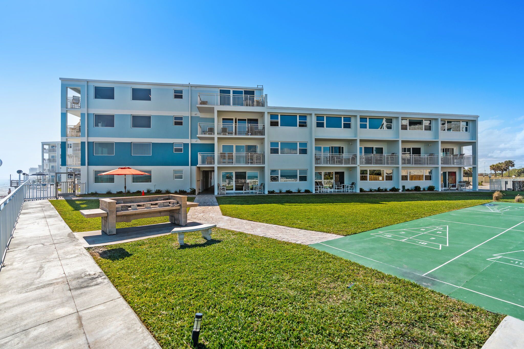 A multi-story residential building with balconies, a green lawn, and a shuffleboard court.