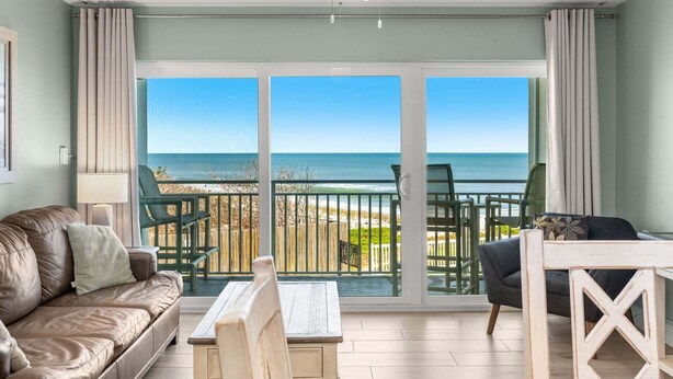 A room with a view of the ocean, a ceiling fan, a sofa, a table, and a chair. - Paradise Beach Club - Direct Oceanfront Condos with Heated Pool Pet-Friendly (Satellite Beach)