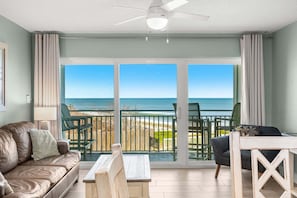 A room with a view of the ocean, a ceiling fan, a sofa, a table, and a chair. - Paradise Beach Club - Direct Oceanfront Condos with Heated Pool Pet-Friendly (Satellite Beach)