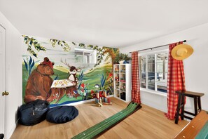 Una habitación con un mural, una ventana con cortinas, una estantería y un felpudo en el suelo.