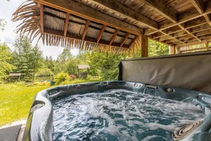 A hot tub with a wooden roof and a grassy area with trees and a small building in the background. - Waterfront 4BR Chalet: Hot Tub, Kayak, 1h MTL (Chertsey)