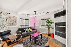 Una sala de estar moderna con chimenea, un letrero de neón y un ventanal grande.
