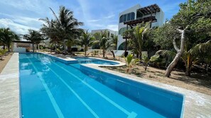 Una piscina de diseño moderno, rodeada de palmeras y un edificio blanco con amplias ventanas.