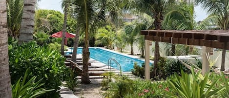 A pool area with palm trees, a red umbrella, and a pergola.