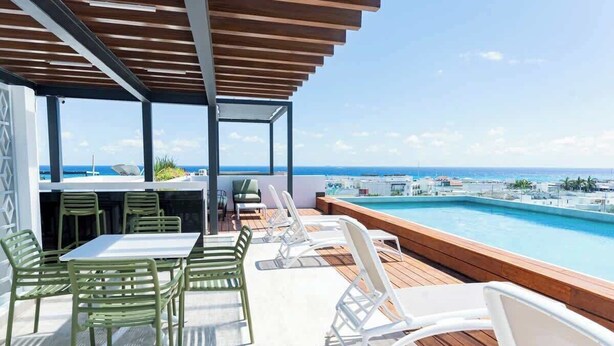 A rooftop terrace with a pool, outdoor seating, and a view of the ocean. - Playa Studio: Rooftop Pool, Steps to 5th Avenue (Playa del Carmen)