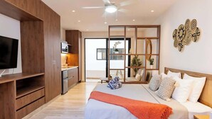 A modern bedroom with a bed, bedside table, and a TV on a wooden cabinet. - Playa Studio: Rooftop Pool, Steps to 5th Avenue (Playa del Carmen)