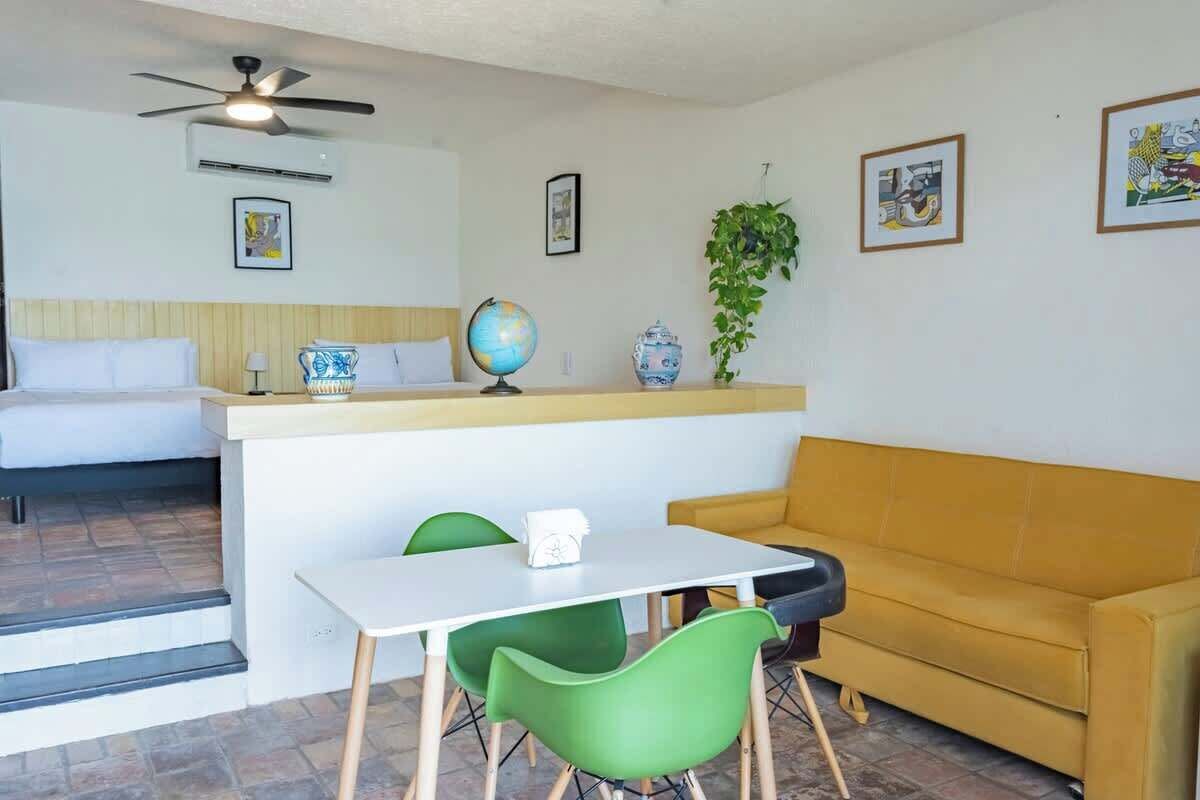 A compact living space with a bed, a sofa, a dining table with chairs, a ceiling fan, a globe, and a plant.