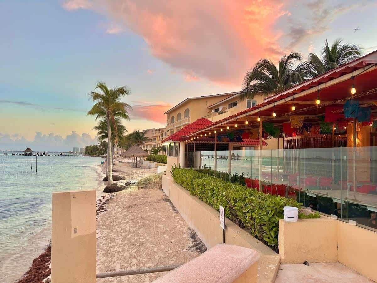 Een hotel aan het strand met een zwembad, palmbomen en uitzicht op de zonsondergang.
