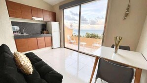 Un espacio habitable moderno con cocina, comedor y un amplio ventanal corredera que da a un balcón con vistas.