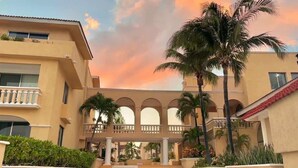 Un hotel con un patio central, palmeras y un cielo al atardecer.