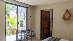 Un dormitori amb un llit, una taula de dinar amb cadires, un finestral gran i una porta que dona a una zona exterior.