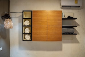 Ein an der Wand befestigtes Holzschränkchen mit vier Ablagen, auf denen jeweils ein aufgerolltes weißes Handtuch liegt.