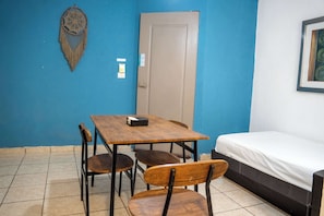 A small room with a blue wall, a bed, a table with chairs, and a door. - Central Cancun Apt - Shared Rooftop Terrace (Cancún)