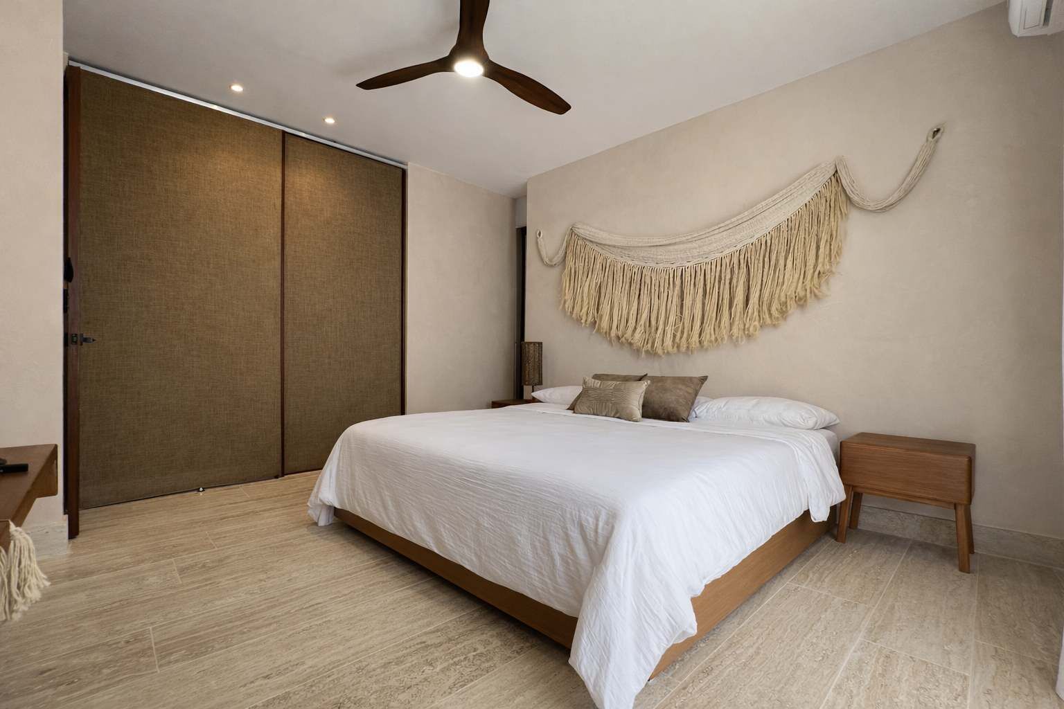 A bedroom with a bed, wooden floor, ceiling fan, and a large wall hanging.