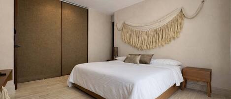 A bedroom with a bed, wooden floor, ceiling fan, and a large wall hanging.