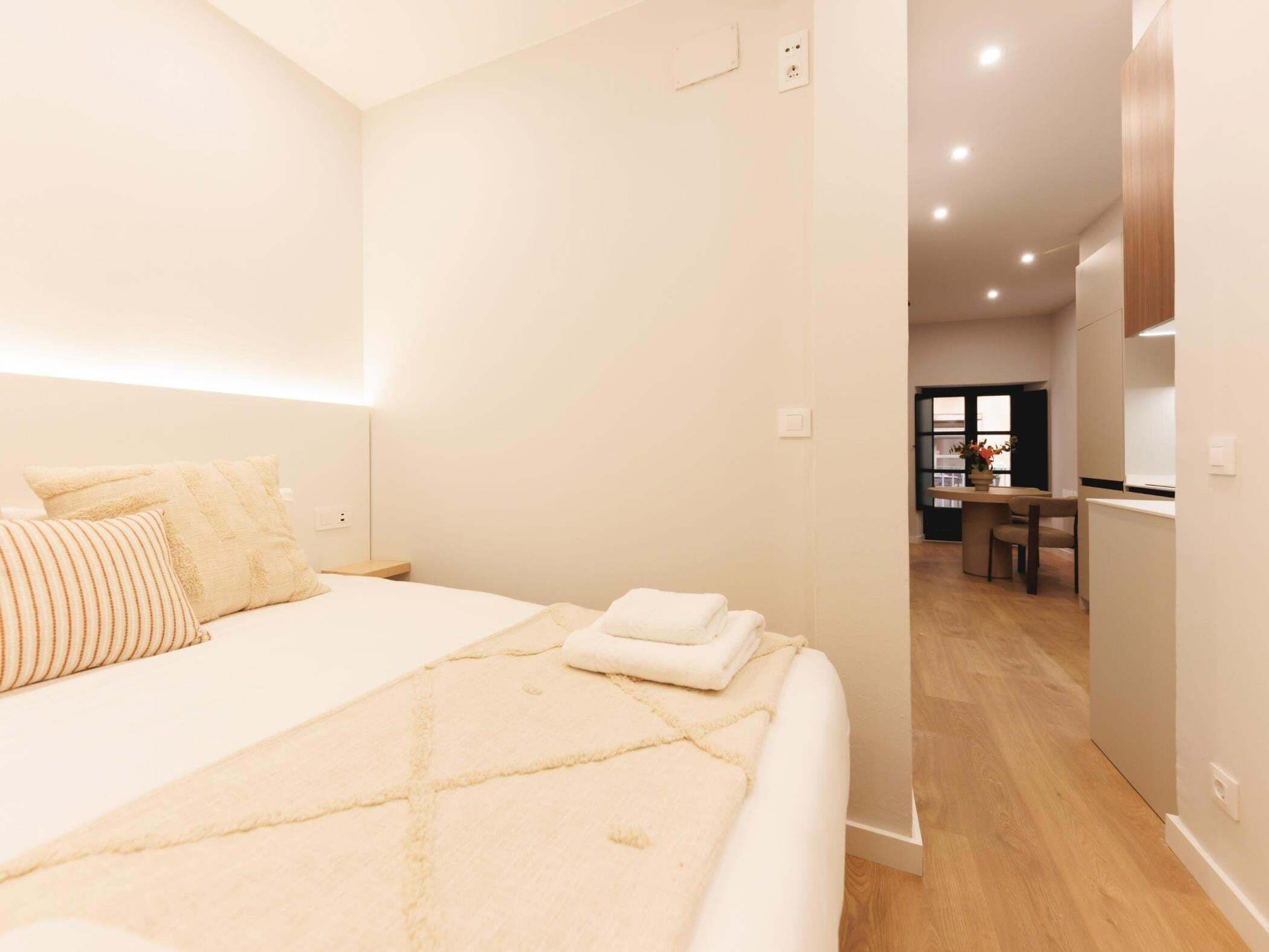 Quarto moderno com cama grande, mesa de cabeceira e vista para a sala de jantar.
