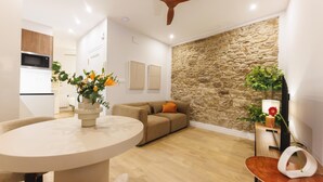 Un espacio habitable moderno con una pared de piedra, una mesa redonda de comedor, un sofá y un ventilador de techo.