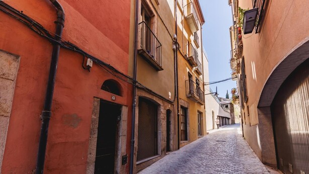 Una estrecha calle empedrada bordeada por edificios con puertas arqueadas y balcones.