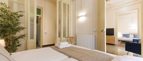 A hotel room with a bed, a radiator, a TV, a desk, and a chair.