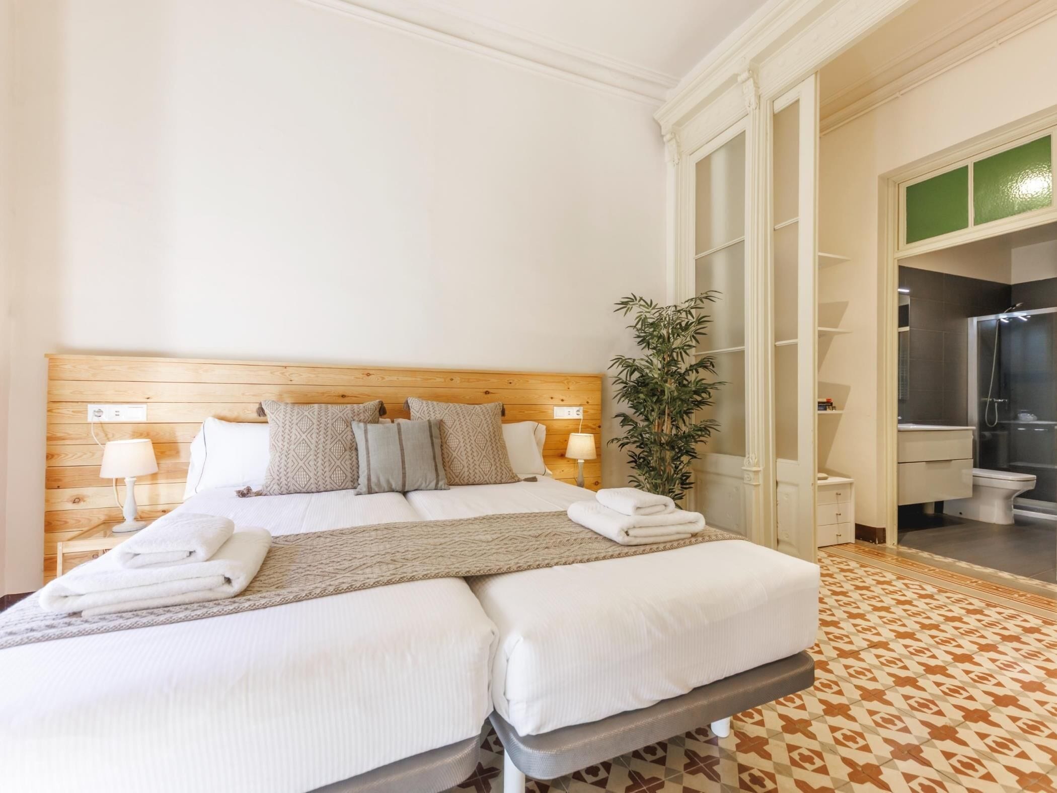 Ein Doppelbett mit Holzkopfseitenverkleidung, zwei Nachttischlampen, ein Blumentopf und ein Badezimmer mit Dusche und Toilette.
