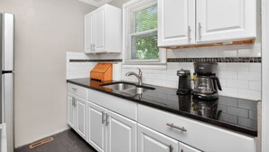 A kitchen with white cabinets, a black countertop, a sink, a coffee maker, and a window with blinds. - Cottage, Great Location Downtown / Airport 4 beds (Nashville)