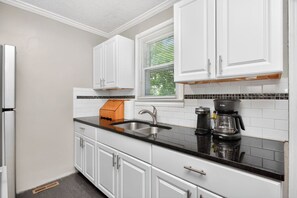A kitchen with white cabinets, a black countertop, a sink, a coffee maker, and a window with blinds. - Cottage, Great Location Downtown / Airport 4 beds (Nashville)