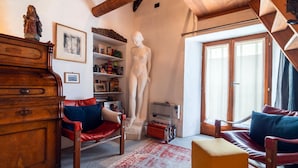 Een gezellige woonkamer met een houten dressoir, een rode leren fauteuil, een wit beeldje en een boekenkast vol boeken en decoratieve objecten.