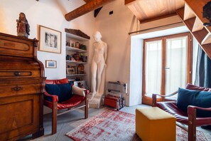 Una sala de estar acogedora con un aparador de madera, un sillón de cuero rojo, una estatua blanca y una estantería llena de libros y adornos.