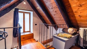 Een houten slaapkamer op zolder met een schuine wand, een raam, een houten trap en een klein nachtkastje met een wereldbol en boeken.