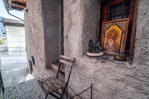 Un edificio de piedra con un banco de madera afuera, una ventana con una pintura religiosa colorida y una pequeña planta en el alféizar.