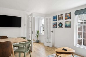 A room with a dining table, chairs, a TV, a door, and artwork on the wall. - Modern Mews House in Central Totnes (Devon)